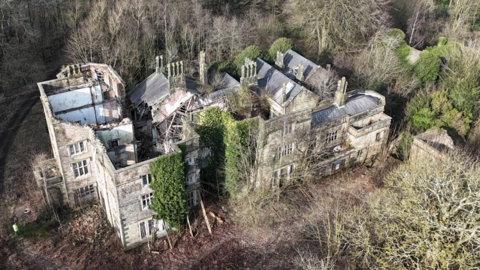 Photograph of Winstanley Hall in Wigan. The image shows an overgrown, derelict building, with collapsed walls and no roof.