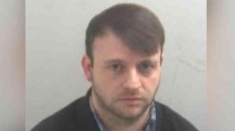 Conor Brady has dark hair, dark eyes and is wearing a shirt and a black jacket.