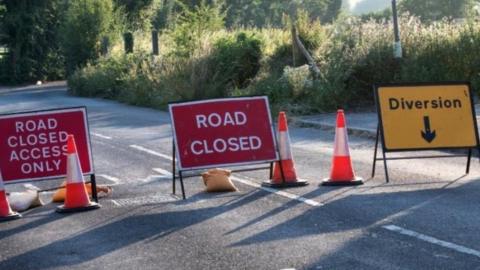 Road closed signs and cones across a road - it is a sunny day