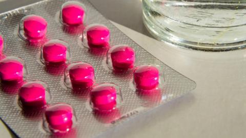 A packet of pink tablets, on a counter, by a glass of water. 