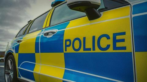 A close up shot of the side of a Northumbria Police car. It is patterned with blue and yellow squares.
