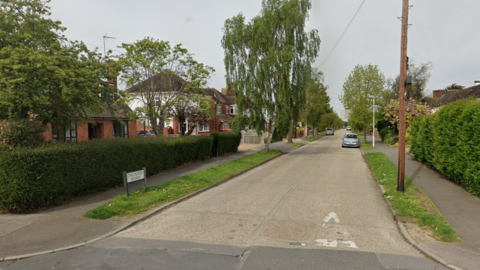 Chelmerton Avenue, showing a road, road sign, green verges either side, hedging around front gardens and detached houses 