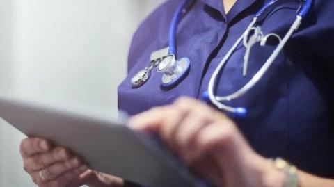 The torso of a female nurse, as she works what appears to be a tablet or an ipad.