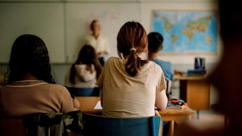 Stock image of teenagers in a clasroom and teacher at the front