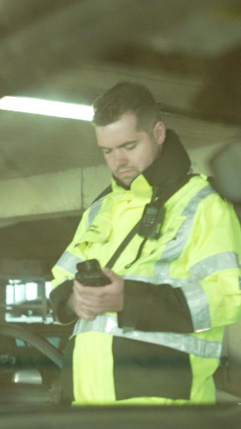 A parking warden in a hi-viz jacket looking at a phone.