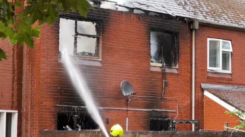 A two-storey house that has been blasted with water. Its roof has caved in because of the fire and the window