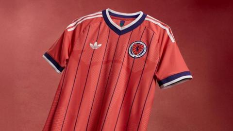 Salmon-pink Scotland shirt with dark purple pinstripes and white Adidas stripes down the shoulders and sleeves.