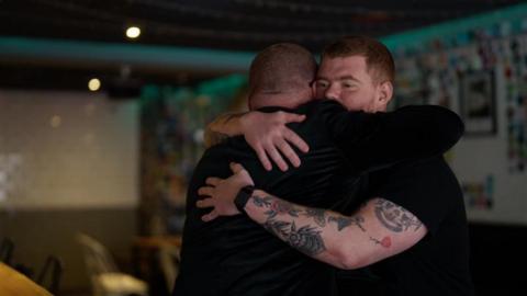 Heston Blumenthal and his son embrace, both wearing black. 