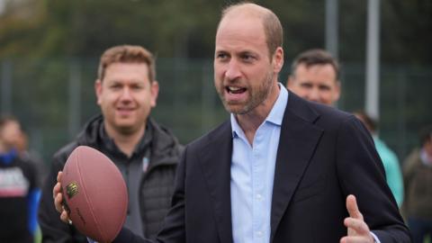 Prince William holds an American football in his hand