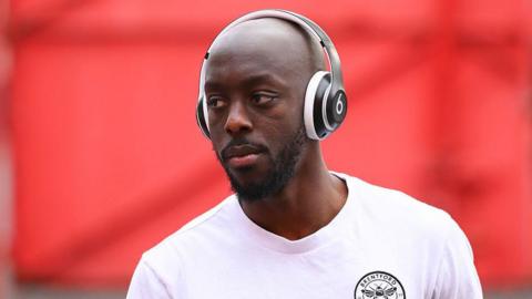 Yoane Wissa wears headphones and wears a white Brentford T-shirt