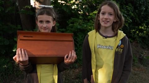 Two children. One of them is holding a box.