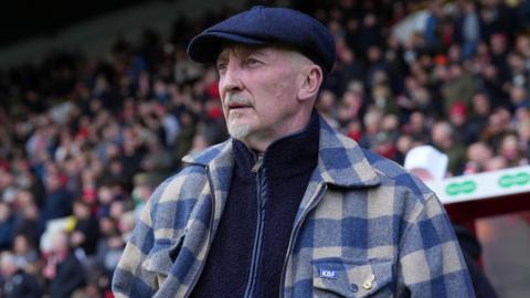Ian Holloway, wearing a navy blue flat cap and a beige and blue checked overshirt, with a navy blue fleece underneath