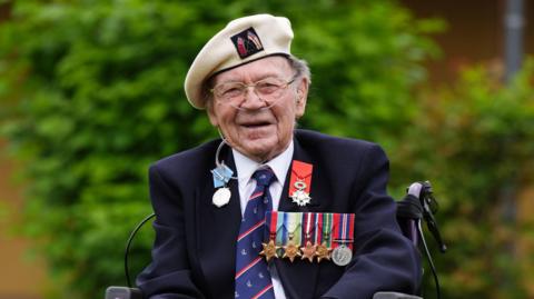 Albert Lamond smiling at the camera. He is wearing a white military hat and a blue blazer with a collection of medals on the upper right chest.