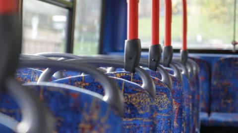 An empty bus with blue seats and red handles