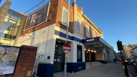 The outside of a red-brick theatre with the word Regent written on the side of a canopy above the main entrance