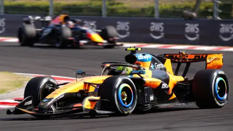 The McLaren of Lando Norris is pushed into position by his mechanics on the grid before the start of the Hugarian Grand Prix