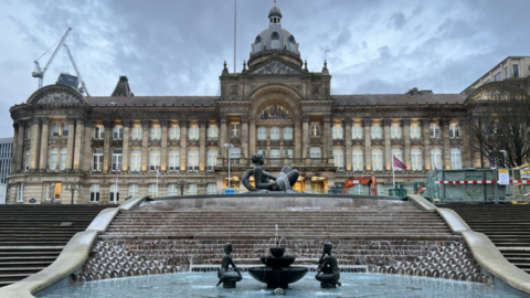 Fountains and steps leading up to the Birmingham City Council building on Victoria Square are in the bottom half of the image. The building with many windows across three levels is in the top half.