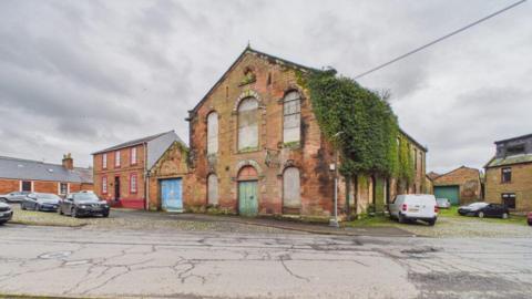 A derelict sandstone building with a lot of vegetation growing out of the side of it