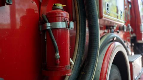 A stock image of the side of a red fire engine. The hose, attached to the side of the vehicle, is at the forefront of the picture. 