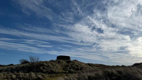 Blue sky streaked with white clouds over a grassy moor with rectangular monument