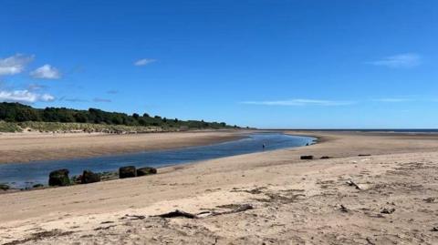 The River Aln as it approaches the sea across a sandy beach