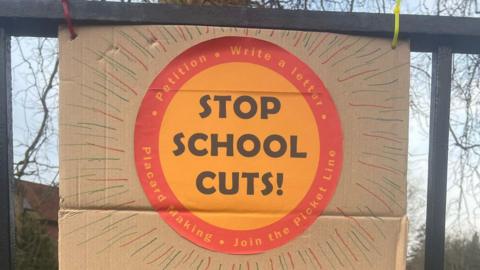 A home-made placard reads 'stop school cuts'.