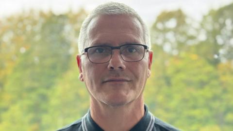 Paul Haywood, a middle-aged white man with short, blonde hair and rectangular glasses with black frames. 