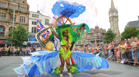 Woman dressed in a colourful costume as part of the Leicester Caribbean Carnival troops in the parade near the clocktower in the city centre