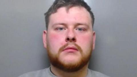 Mugshot of Gavin Jackson. He has short dark hair and a thick ginger beard.