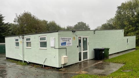 The outside of Copthorne Guide and Scout HQ. The building is painted mint green and has white doors and windows. 