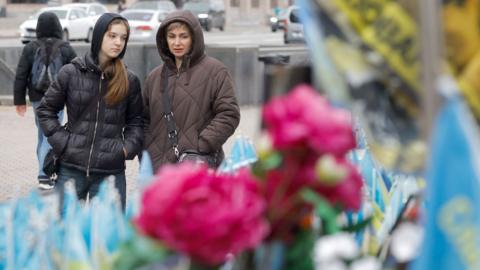 A woman and girl look at flags and tributes at a makeshift memorial in the Independence Square, Kyiv, Ukraine, 20 October 2025