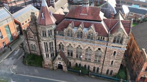 A drone view of the Derby School of Art, which is a three-storey Victorian building with ornate windows and a steeple. The roof is made of red tile.