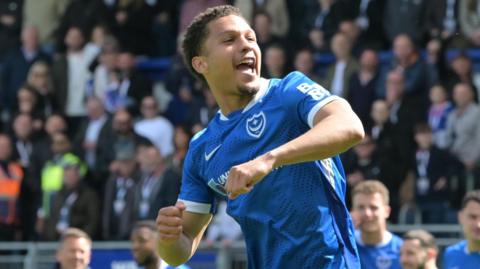 Ibane Bowat, wearing Portsmouth's blue home shirt, celebrates at full-time against Leicester by punching his fists in the air with his mouth open while shouting.