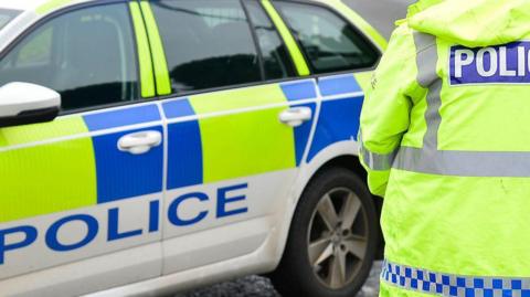 Police car with police officer's back in the side of the shot in a yellow police coat 