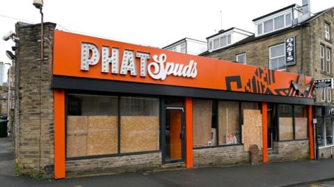 A takeaway with boarded-up windows and orange signage