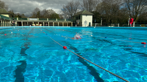 Peterborough Lido, with clear blue water and a swimmer splashing while moving along a lane in the pool