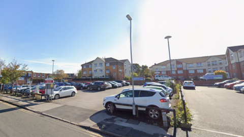 Entrance to a car park with a three storey building behind and blue sky above