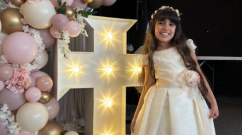 Alice da Silva Aguiar smiles at the camera wearing her white Communion dress