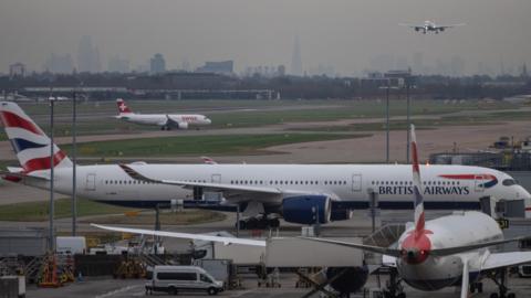 Planes on a runway with another plane in the background coming into land.