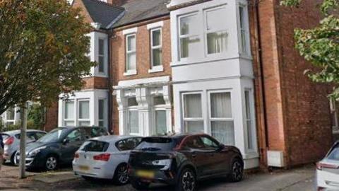Exterior of a brick Victorian house with cars parked in front. The windows and sills are painted white
