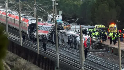 A firefighter and members of the Spanish Civil Guard work next to one of the trains involved in the accident, at the site of a deadly derailment of two high-speed trains near Adamuz, in Cordoba, Spain