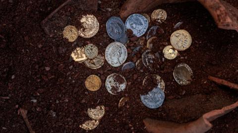The image shows some silver coins in the first, with a broken earthenware pot in the background.