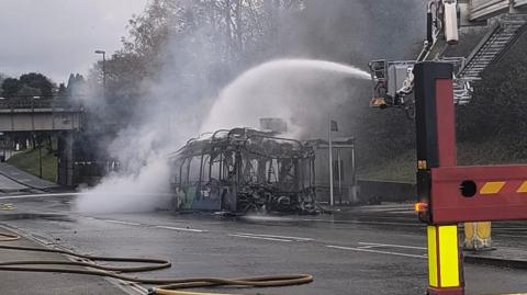 A fire tender hoses down the metal skeleton of a burnt out bus in Crawley.