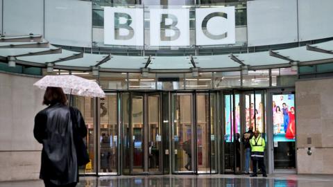 A person walks with an umbrella outside BBC Broadcasting House in London in November 2025