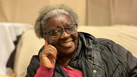 Iona Walker is smiling and wearing a pink jumper and black coat.