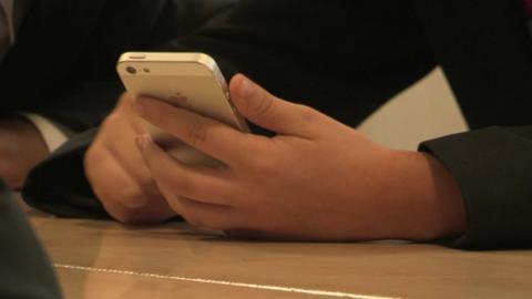 Hands of a schoolboy holding a mobile phone while sat at a desk