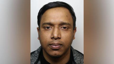 A police profile photo of a man with black hair wearing a grey and black jacket. 