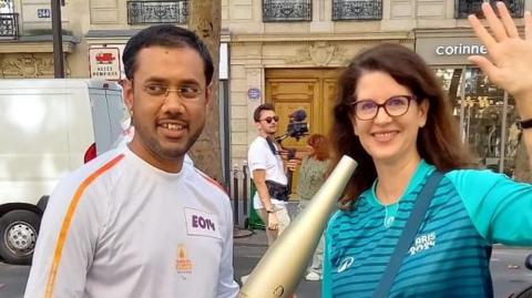 Mohammed Zaman, pictured with volunteer Lucille, wearing his white torchbearer outfit and holding the Olympic torch