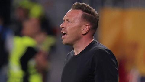 Wales boss Craig Bellamy reacts with an open-mouthed expression as he stands in a round-neck black top