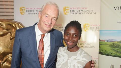 Jon Snow and Dr Precious Lunga smiling in front of a Bafta banner